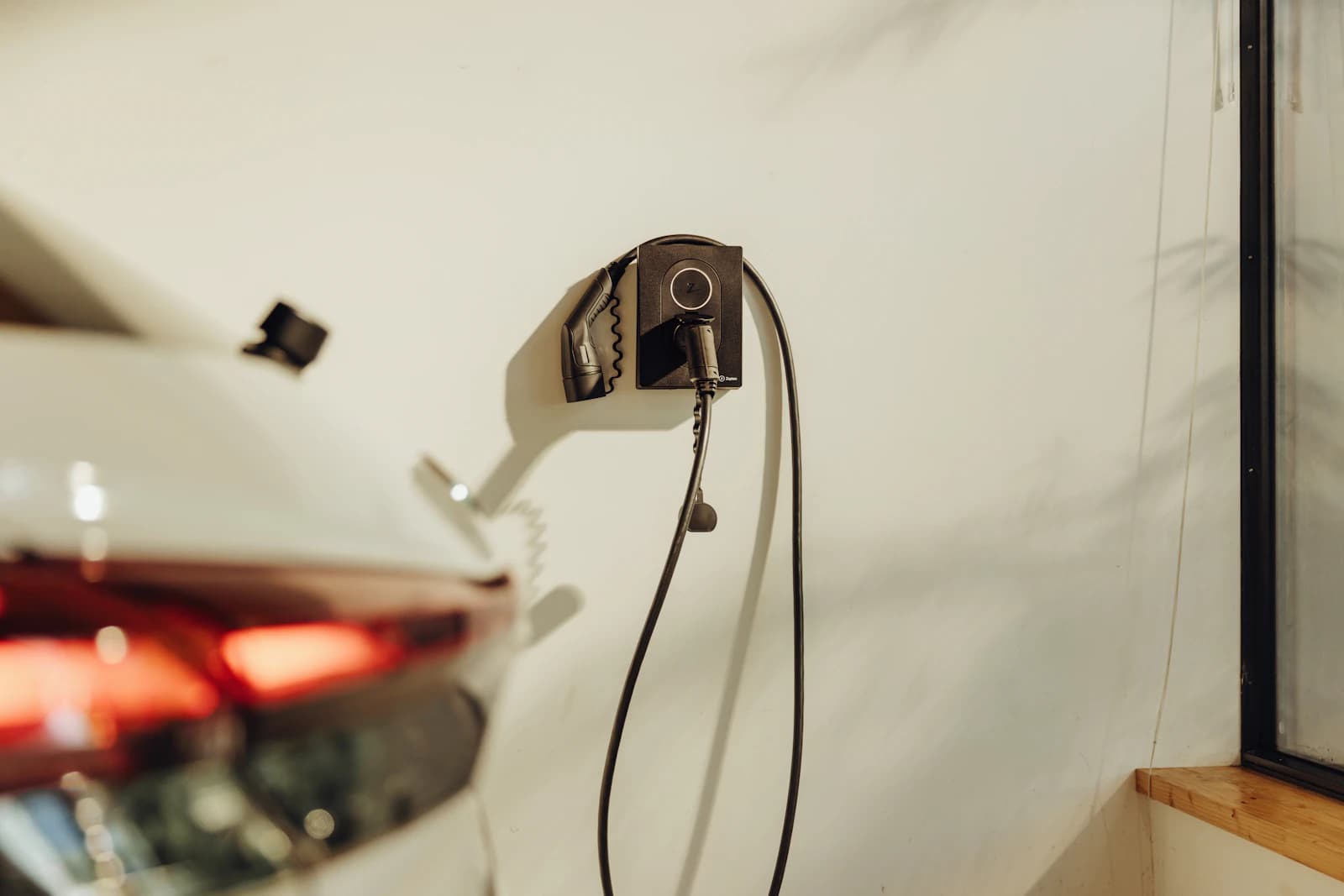 Thuislaadpaal aan de muur naast geparkeerde elektrische auto in een Nederlandse oprit