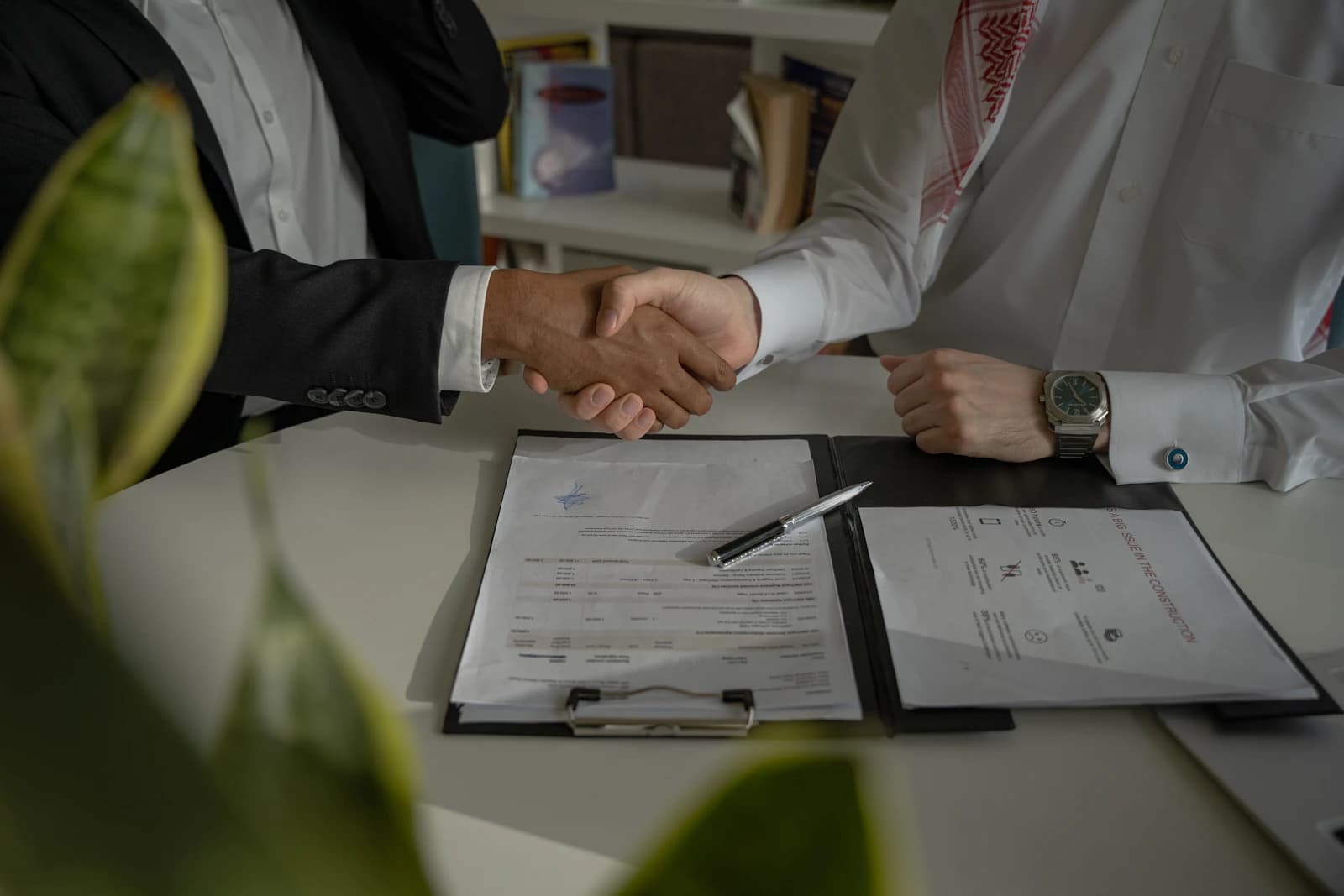 Vakman en klant geven elkaar een hand boven een ondertekende offerte met garantievoorwaarden